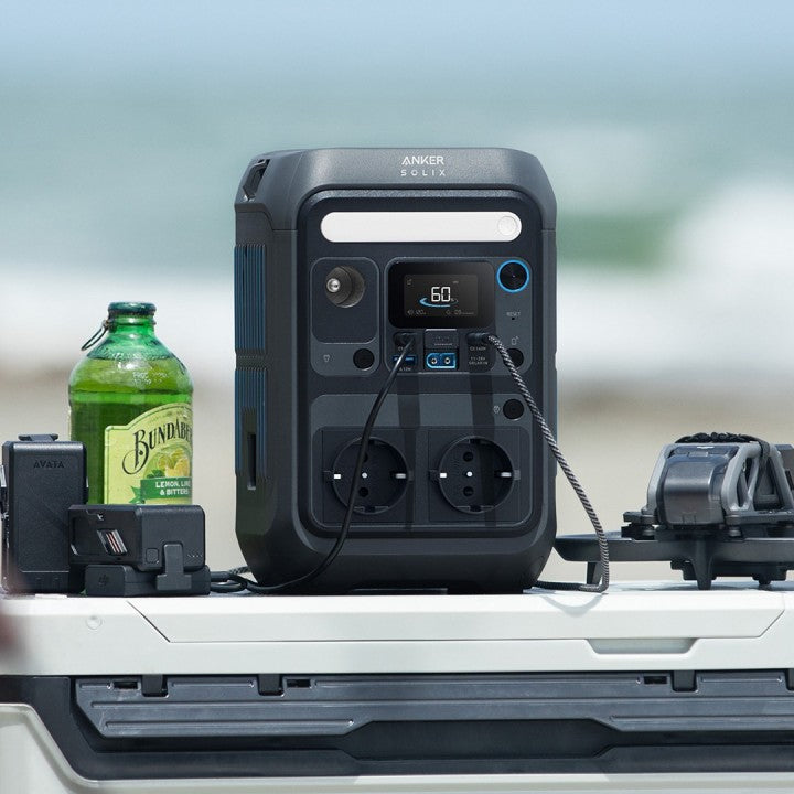 Anker SOLIX C300X 288Wh Power Bank on a table with drinks and electronics, perfect for outdoor use.