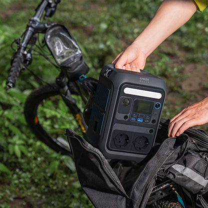 Anker SOLIX C300X 288Wh Power Bank being held next to a mountain bike in a green outdoor setting.