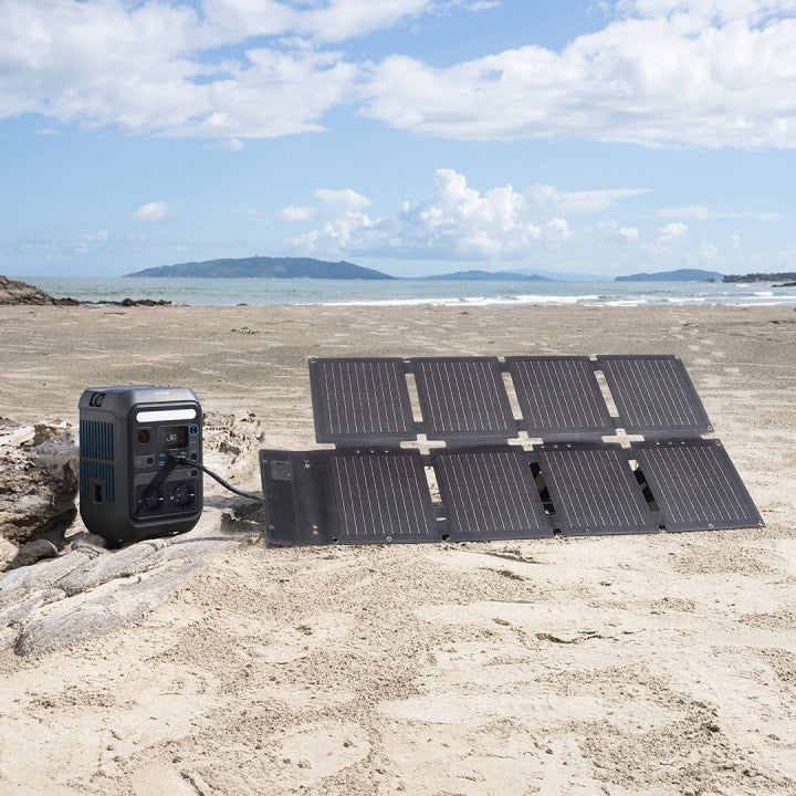 Anker SOLIX C300X 288Wh Power Bank next to solar panels on a sandy beach with a scenic backdrop.