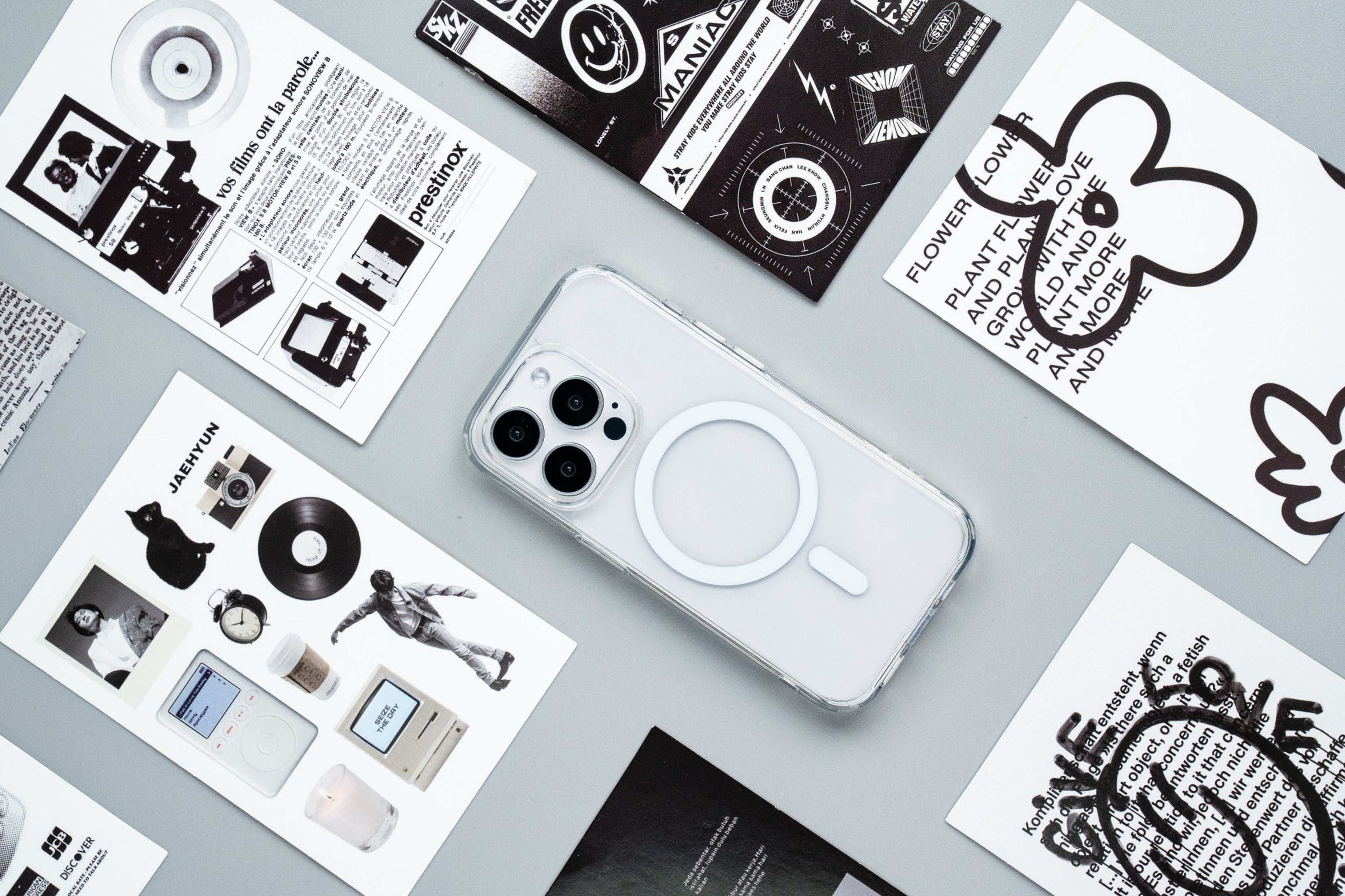 White smartphone with MagSafe ring on a gray surface with graphic design sheets.