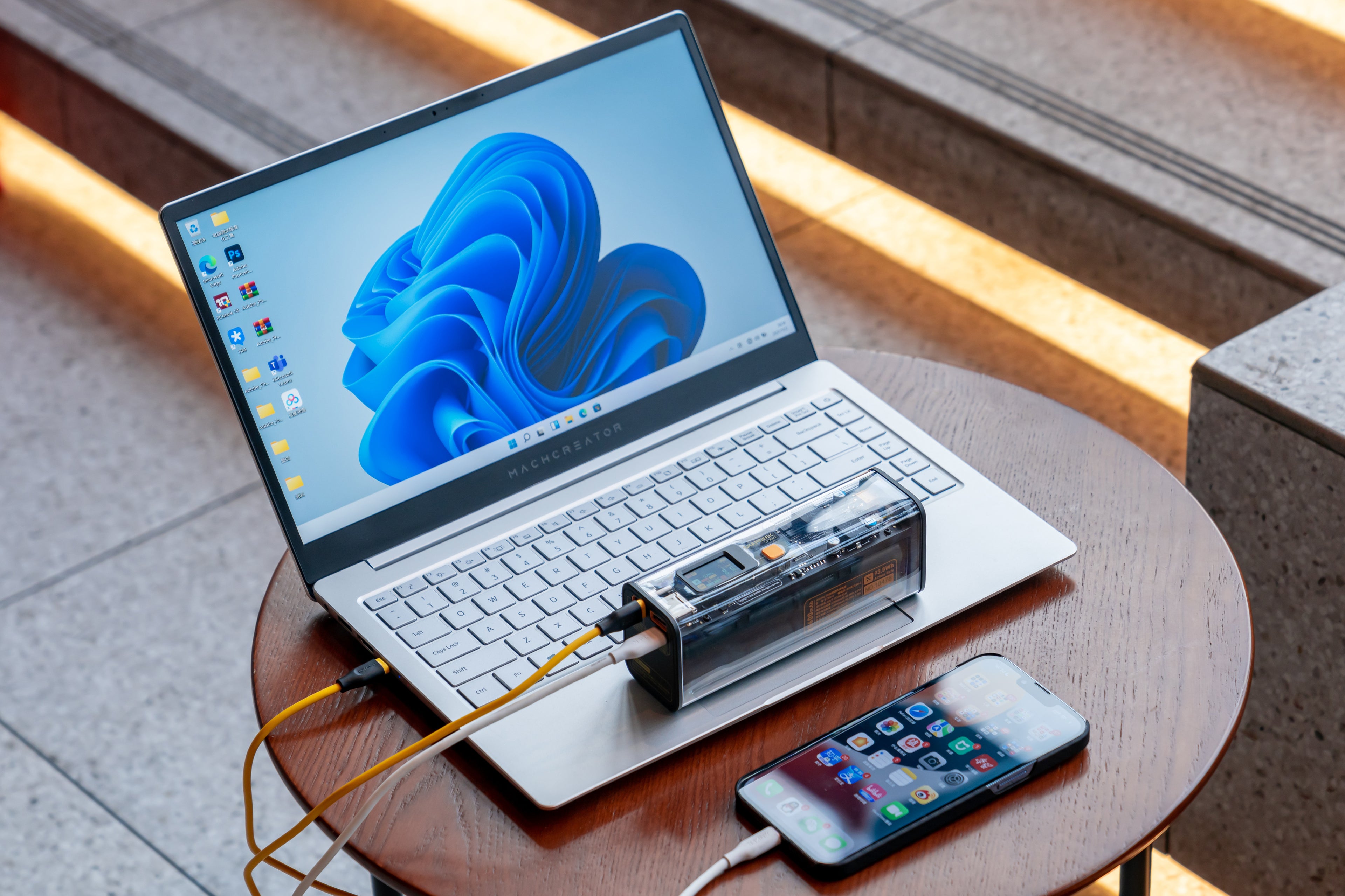 SHARGE Shargeek 100 Powerbank charging laptop and smartphone on a wooden table, showcasing transparent design and fast charging.