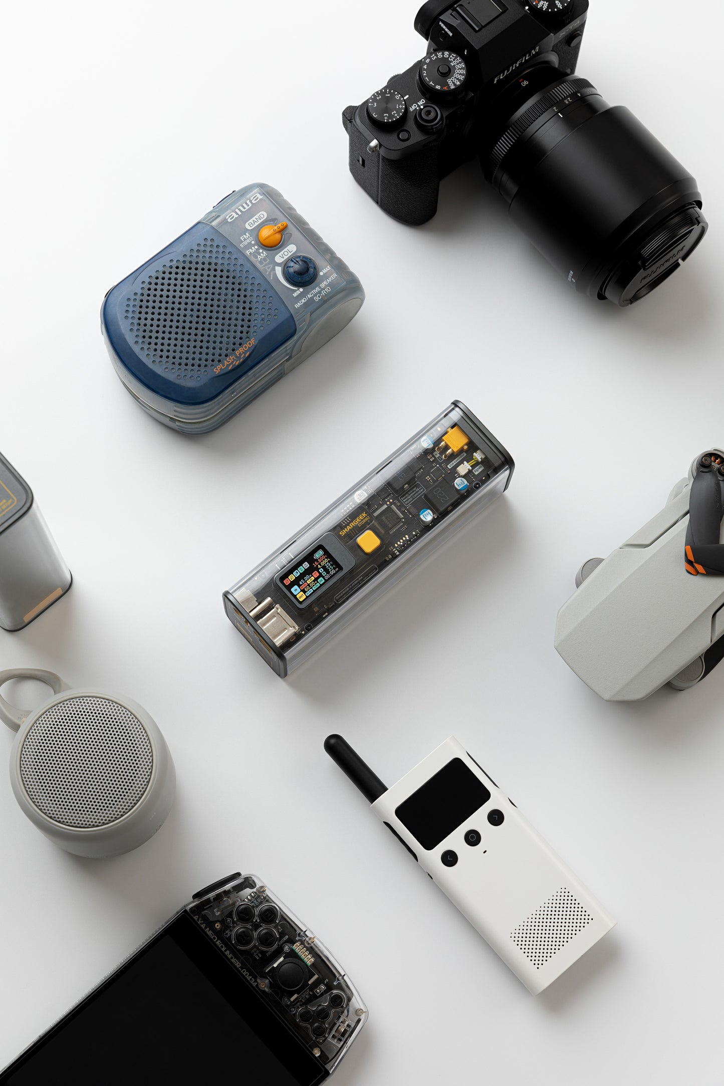 Collection of tech gadgets including a transparent powerbank, cameras, and portable speakers on a white background.